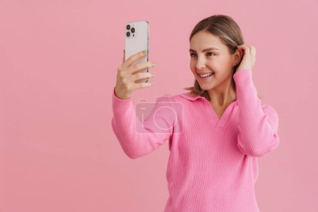 Téléchargez les photos : Jeune belle femme blanche souriante et prenant selfie photo sur téléphone portable debout isolé sur fond rose - en image libre de droit