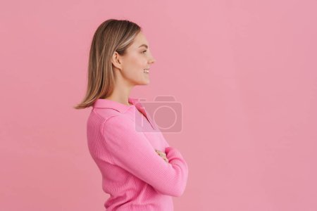 Foto de Joven hermosa chica sonriente con los brazos cruzados de pie con su lado derecho sobre el fondo rosa aislado - Imagen libre de derechos