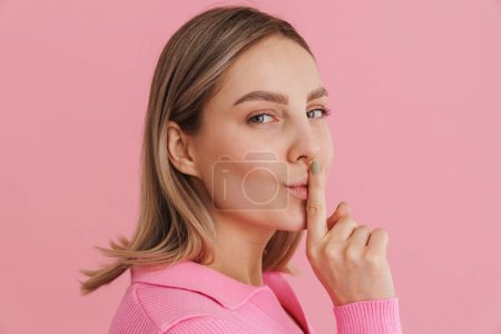 Photo for Portrait of young beautiful girl showing silence gesture looking in camera and standing with her right side over isolated pink background - Royalty Free Image