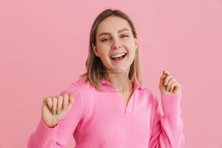 Photo for Young happy smiling girl in pink blouse dancing and opened mouth over isolated pink background - Royalty Free Image