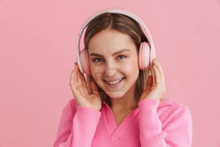 Photo for Young beutiful smiling girl enjoying music in pink headphones looking on camera over isolated pink background - Royalty Free Image
