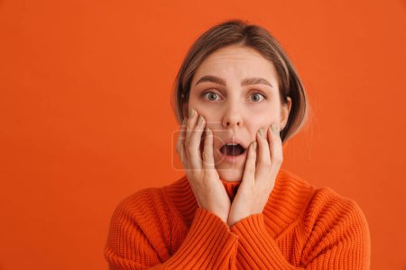 Photo for Young surprised girl touching her cheeks with opened mouth over isolated orange background - Royalty Free Image