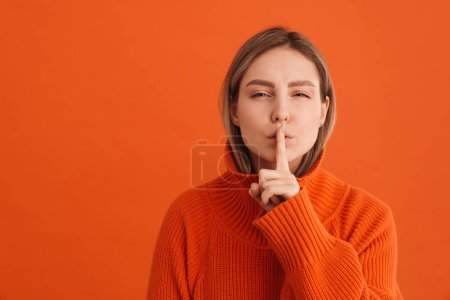 Téléchargez les photos : Jeune femme blanche tenant son doigt à la bouche et faisant un geste de silence debout isolé sur fond rouge - en image libre de droit