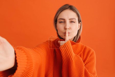 Téléchargez les photos : Jeune femme blanche tenant son doigt à la bouche et prenant selfie photo debout isolé sur fond rouge - en image libre de droit
