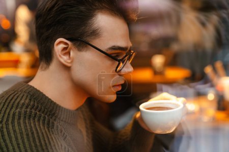 Foto de Joven morena blanca hombre serio con anteojos bebiendo café en la cafetería - Imagen libre de derechos