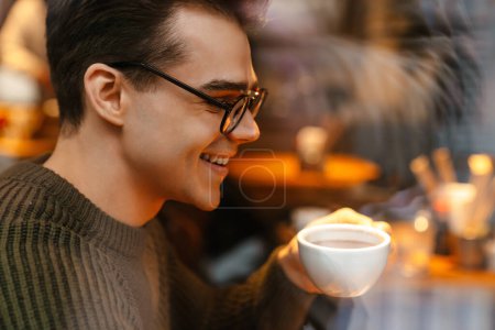 Foto de Joven morena blanca con anteojos sonriendo mientras bebe café en la cafetería - Imagen libre de derechos