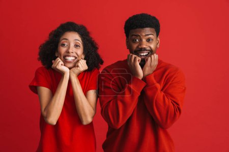 Téléchargez les photos : Noir heureux homme et femme souriant et regardant caméra isolé sur fond rouge - en image libre de droit
