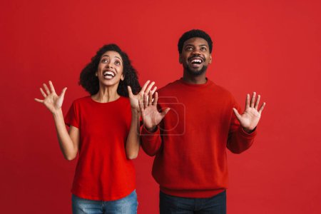 Téléchargez les photos : Noir heureux homme et femme souriant et montrant leurs paumes isolées sur fond rouge - en image libre de droit