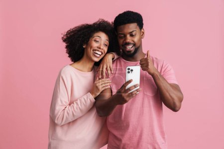 Téléchargez les photos : Noir heureux homme et femme souriant et gestuelle au téléphone cellulaire isolé sur fond rose - en image libre de droit
