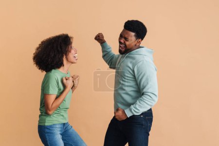 Téléchargez les photos : Homme et femme noirs riant et gesticulant comme des gagnants isolés sur fond beige - en image libre de droit