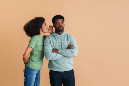 Photo for Black happy woman smiling and whispering secret at man's ear isolated over beige background - Royalty Free Image