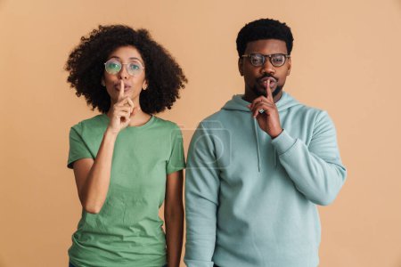Téléchargez les photos : Homme et femme noirs portant des lunettes faisant un geste de silence isolé sur fond beige - en image libre de droit
