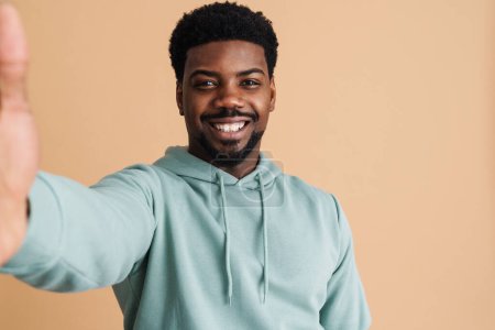 Photo for Black bearded young man smiling and taking selfie photo isolated over beige background - Royalty Free Image