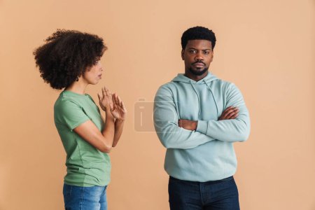 Téléchargez les photos : Femme noire exprimant son insatisfaction et faisant un geste d'arrêt tout en regardant l'homme isolé sur fond beige - en image libre de droit