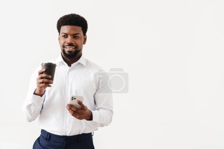 Téléchargez les photos : Noir mi-homme portant chemise boire du café tout en utilisant un téléphone cellulaire isolé sur fond blanc - en image libre de droit