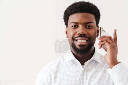 Téléchargez les photos : Homme barbu noir portant une chemise utilisant un téléphone portable isolé sur fond blanc - en image libre de droit