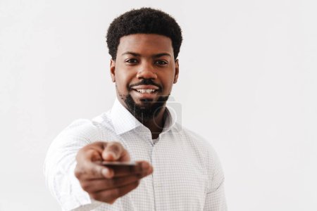 Téléchargez les photos : Noir mi-homme souriant et montrant la carte de crédit à la caméra isolé sur fond blanc - en image libre de droit