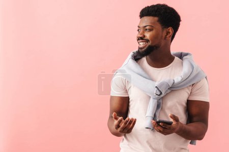 Photo for Black mid man wearing t-shirt smiling while using mobile phone isolated over pink background - Royalty Free Image