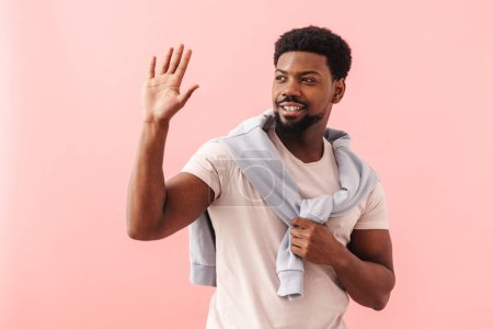 Photo for Black mid man wearing t-shirt smiling and waving hand isolated over pink background - Royalty Free Image