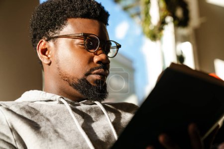 Téléchargez les photos : Noir barbu livre de lecture tout en étant assis dans un café à l'intérieur - en image libre de droit
