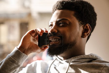 Photo for Black bearded man talking on mobile phone and smiling in cafe indoors - Royalty Free Image