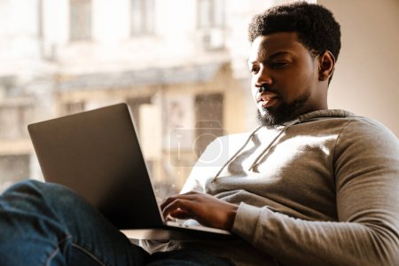Téléchargez les photos : Homme barbu noir travaillant avec un ordinateur portable tout en étant assis dans un café à l'intérieur - en image libre de droit