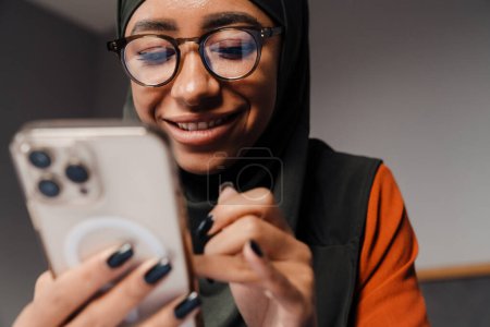Foto de Joven hermosa mujer sonriente en hijab y gafas con teléfono - Imagen libre de derechos