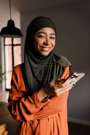 Téléchargez les photos : Jeune belle femme souriante heureuse en hijab avec téléphone regardant la caméra - en image libre de droit