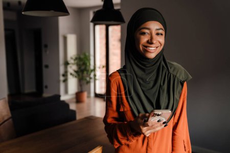 Foto de Joven hermosa mujer sonriente feliz en hijab con teléfono mirando a la cámara - Imagen libre de derechos