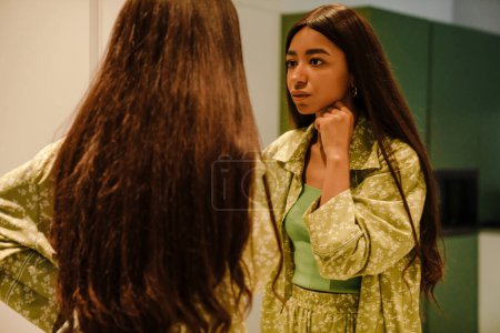 Téléchargez les photos : Jeune belle femme aux cheveux longs se regardant dans le miroir à la maison - en image libre de droit