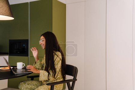 Photo for Young beautiful long haired woman smiling and waving at laptop camera during video conference at home - Royalty Free Image