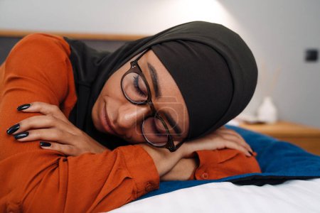 Téléchargez les photos : Jeune belle femme en hijab et lunettes dormant sur le lit - en image libre de droit