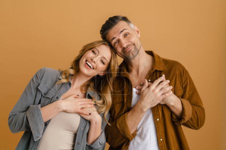 Téléchargez les photos : Blanc heureux femme et homme souriant et gardant les mains au cœur debout isolé sur fond jaune - en image libre de droit