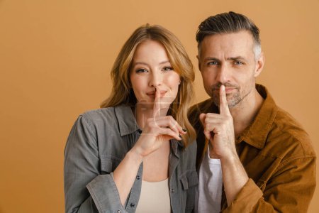 Photo for White happy woman and man smiling and keeping fingers at mouths standing isolated over yellow background - Royalty Free Image