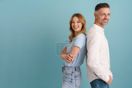 Foto de Blanco feliz hombre y mujer sonriendo mientras que de pie espalda con espalda aislado sobre fondo azul - Imagen libre de derechos