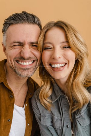 Téléchargez les photos : Blanc couple heureux portant chemises riant et regardant caméra isolé sur fond beige - en image libre de droit
