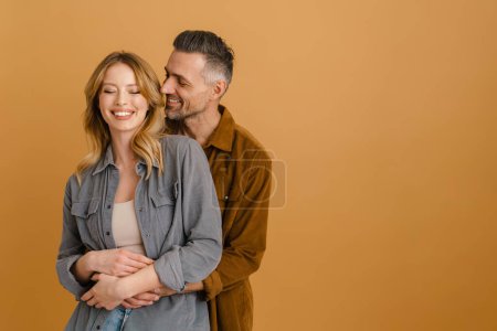 Téléchargez les photos : Blanc couple heureux portant chemises riant et étreignant isolé sur fond beige - en image libre de droit