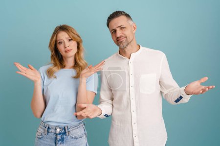 Téléchargez les photos : Blanc mécontent couple fronçant les sourcils tout en gesticulant à la caméra isolé sur fond bleu - en image libre de droit