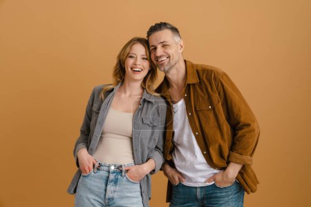 Téléchargez les photos : Blanc couple heureux portant des chemises souriant et regardant la caméra isolé sur fond beige - en image libre de droit