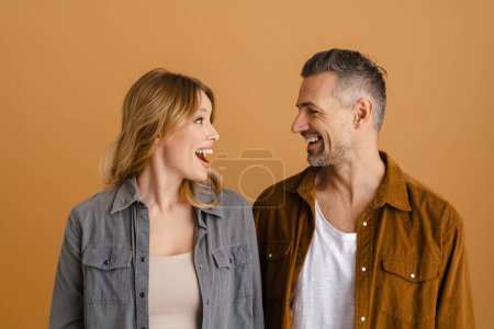 Téléchargez les photos : Couple blanc portant des chemises souriantes et se regardant isolées sur fond beige - en image libre de droit