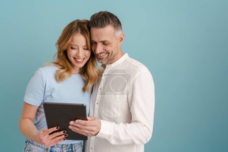 Téléchargez les photos : Blanc heureux couple étreinte et en utilisant tablette isolée sur fond bleu - en image libre de droit