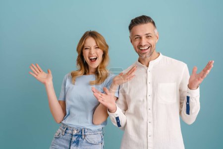 Téléchargez les photos : Blanc excité couple rire tout en gesticulant à la caméra isolé sur fond bleu - en image libre de droit