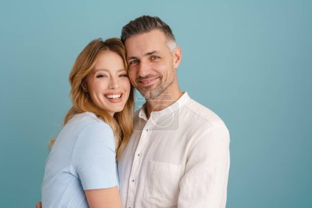 Téléchargez les photos : Blanc couple heureux étreignant et regardant la caméra isolé sur fond bleu - en image libre de droit