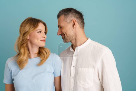 Téléchargez les photos : Blanc heureux couple souriant et regardant l'autre isolé sur fond bleu - en image libre de droit