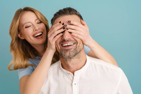 Téléchargez les photos : Ginger femme couvrant les yeux de son petit ami et riant isolé sur fond bleu - en image libre de droit