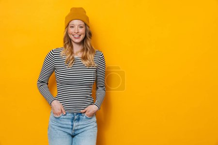 Photo for Young blonde woman wearing hat smiling and looking at camera isolated over yellow background - Royalty Free Image