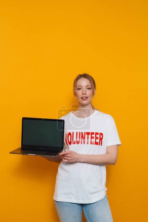Foto de Mujer rubia joven con camiseta que muestra el ordenador portátil aislado sobre fondo amarillo - Imagen libre de derechos