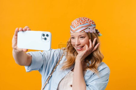 Photo for Young blonde woman smiling and taking selfie on cellphone isolated over yellow background - Royalty Free Image