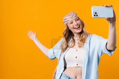 Photo for Young blonde woman gesturing and taking selfie on cellphone isolated over yellow background - Royalty Free Image
