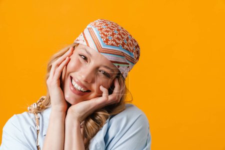 Téléchargez les photos : Jeune femme blonde portant bandanna souriant et regardant la caméra isolée sur fond jaune - en image libre de droit